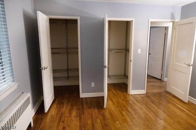 unfurnished bedroom featuring radiator heating unit, wood finished floors, baseboards, and a closet