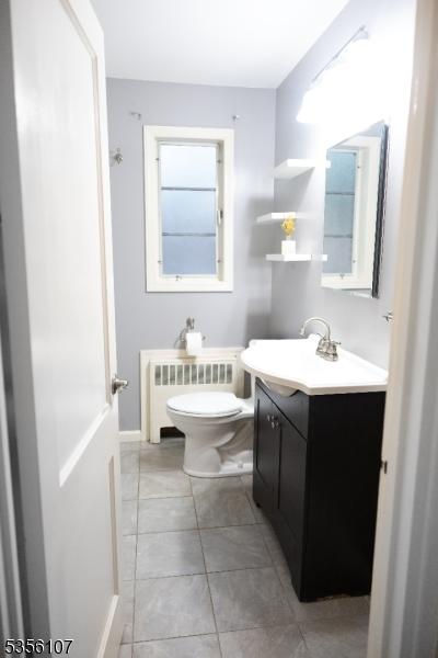 bathroom featuring radiator heating unit, toilet, vanity, tile patterned flooring, and baseboards
