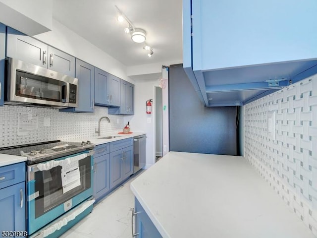 kitchen with appliances with stainless steel finishes, a sink, backsplash, light countertops, and blue cabinets