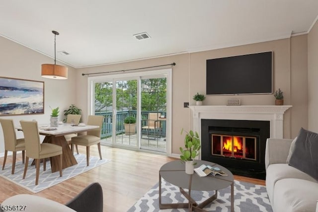 living area with a fireplace with flush hearth, light wood finished floors, crown molding, and visible vents