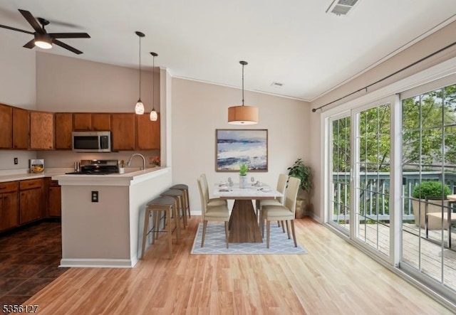 kitchen with ceiling fan, visible vents, stainless steel microwave, brown cabinets, and light countertops
