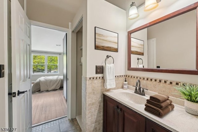 bathroom featuring connected bathroom, tile patterned floors, tile walls, wainscoting, and vanity