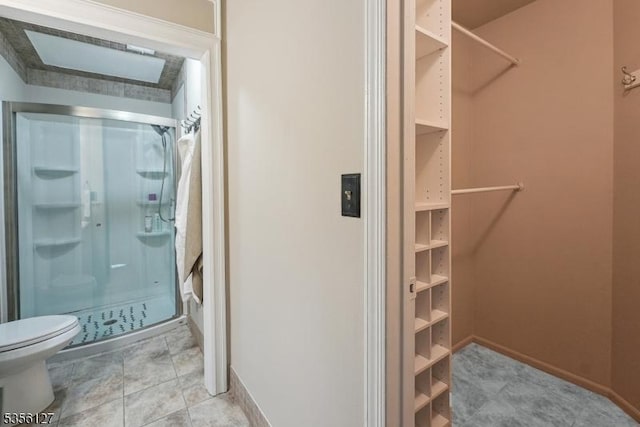 bathroom featuring a stall shower, a spacious closet, toilet, and baseboards