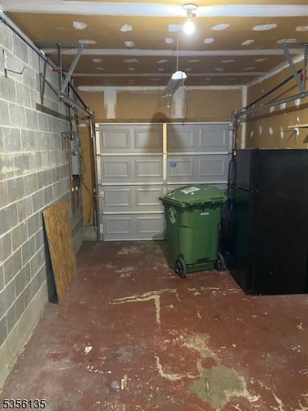 garage with freestanding refrigerator and concrete block wall