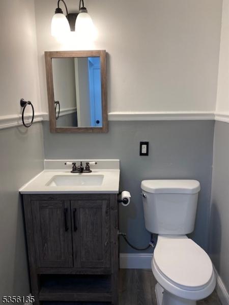 half bath featuring baseboards, vanity, toilet, and wood finished floors