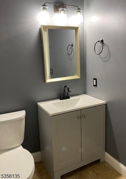 half bath with toilet, baseboards, and vanity