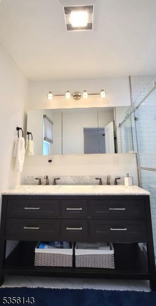 bathroom featuring a stall shower, visible vents, a sink, and double vanity