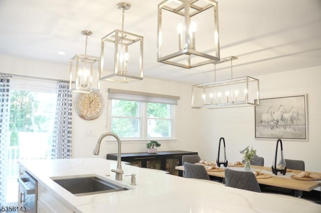 kitchen with light stone countertops, pendant lighting, an inviting chandelier, a sink, and dishwashing machine