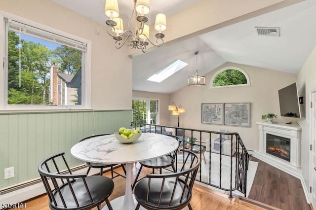 dining room featuring vaulted ceiling, a wainscoted wall, a glass covered fireplace, a chandelier, and a skylight