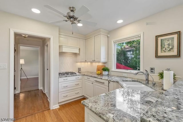 kitchen with a sink, gas stovetop, ceiling fan, light wood-type flooring, and tasteful backsplash