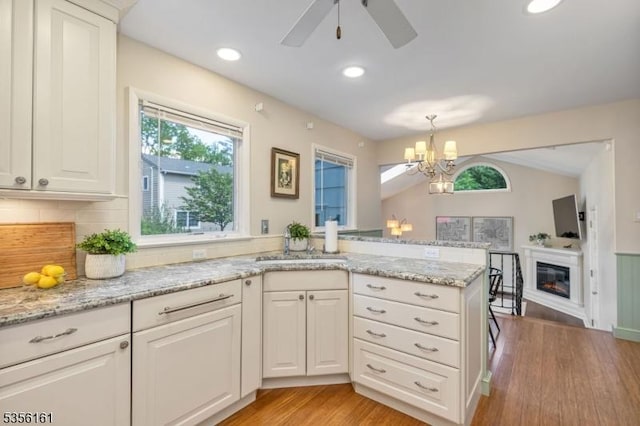 kitchen with a ceiling fan, a peninsula, light wood finished floors, a glass covered fireplace, and a sink
