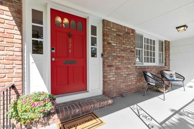 view of exterior entry featuring a porch and brick siding