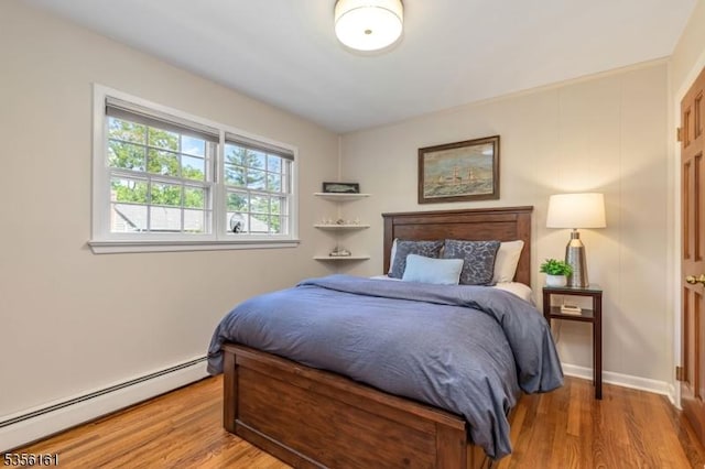bedroom featuring a baseboard heating unit, wood finished floors, and baseboards