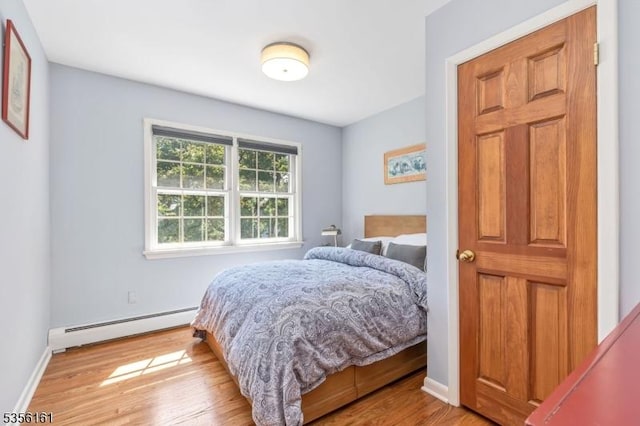 bedroom featuring a baseboard heating unit, wood finished floors, and baseboards