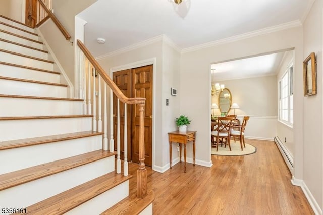 foyer entrance featuring baseboard heating, wood finished floors, stairway, ornamental molding, and baseboards