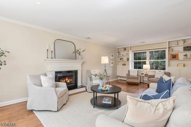 living area with wood finished floors, a glass covered fireplace, ornamental molding, baseboards, and built in shelves