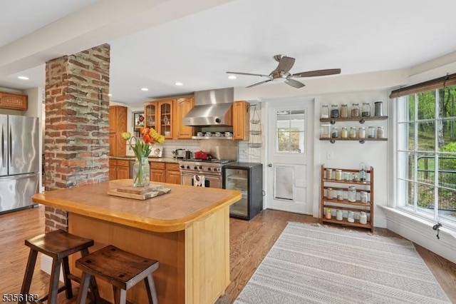 kitchen featuring wall chimney exhaust hood, stainless steel appliances, wood counters, glass insert cabinets, and decorative backsplash