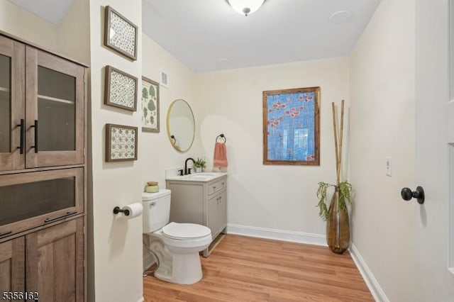 bathroom with toilet, wood finished floors, vanity, and baseboards