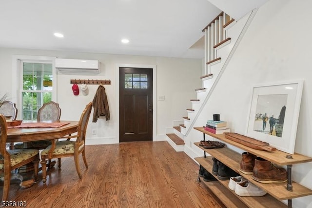 foyer entrance with a wall unit AC, stairs, plenty of natural light, wood finished floors, and recessed lighting