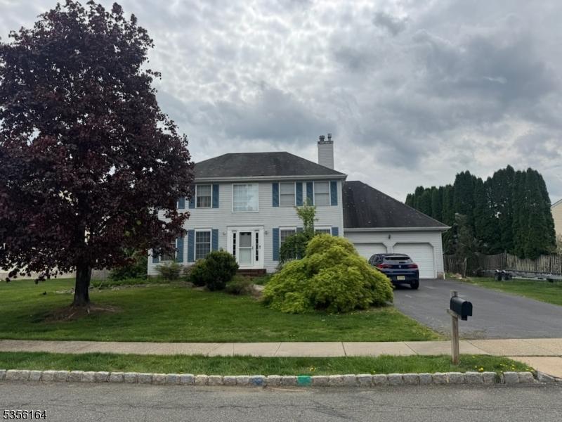 colonial-style house featuring a chimney, driveway, a front lawn, and an attached garage
