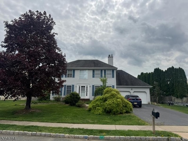 colonial-style house with aphalt driveway, an attached garage, a front lawn, and a chimney