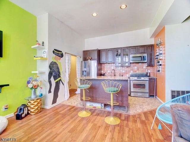 kitchen with decorative backsplash, a breakfast bar area, appliances with stainless steel finishes, and light wood-style flooring