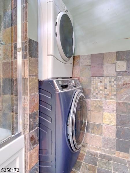 clothes washing area with stacked washing maching and dryer, laundry area, and stone finish floor