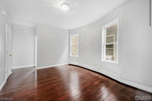 empty room featuring wood-type flooring, baseboard heating, and baseboards