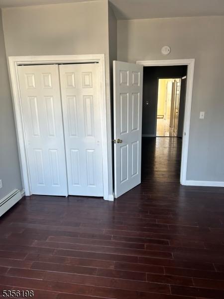 unfurnished bedroom with dark wood-style flooring, baseboards, and a closet