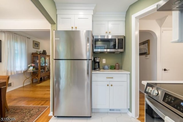 kitchen featuring appliances with stainless steel finishes, white cabinets, light wood-type flooring, and arched walkways