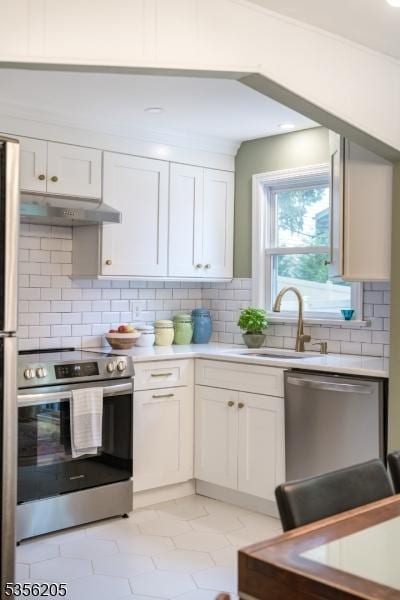kitchen featuring appliances with stainless steel finishes, a sink, under cabinet range hood, light countertops, and white cabinetry