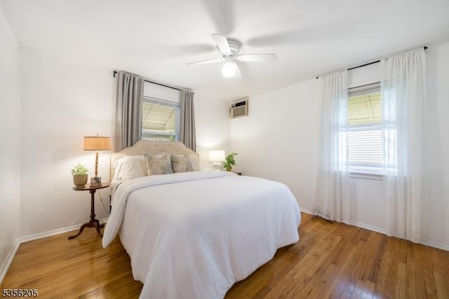 bedroom featuring light wood-style flooring, multiple windows, baseboards, and a wall mounted AC