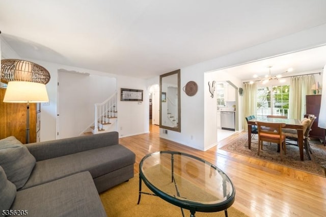 living area featuring light wood-style flooring, stairway, a chandelier, arched walkways, and baseboards