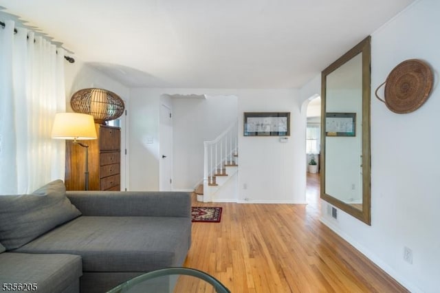 living room featuring wood finished floors, arched walkways, stairs, and baseboards