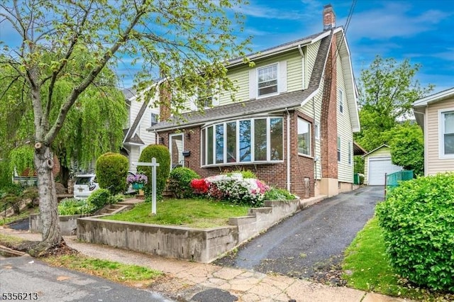 view of front of home featuring an outbuilding, brick siding, a garage, asphalt driveway, and a chimney