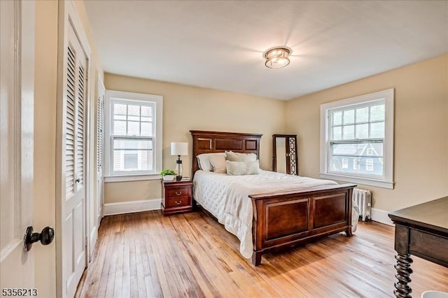 bedroom featuring multiple windows, light wood-style floors, radiator heating unit, and baseboards