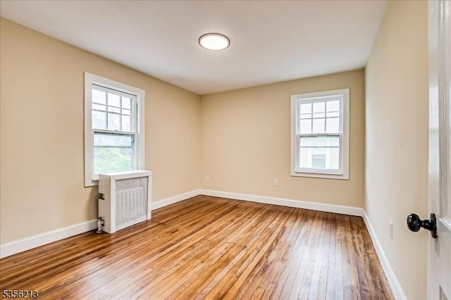 unfurnished room featuring light wood-style flooring, baseboards, and radiator heating unit