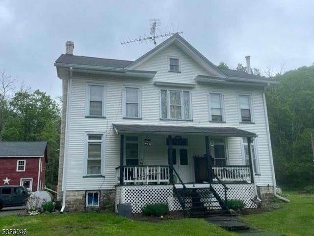 view of front of house featuring a chimney, a porch, and a front lawn