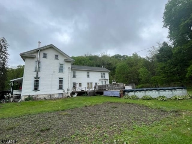 rear view of house featuring a covered pool, a deck, a lawn, and a forest view