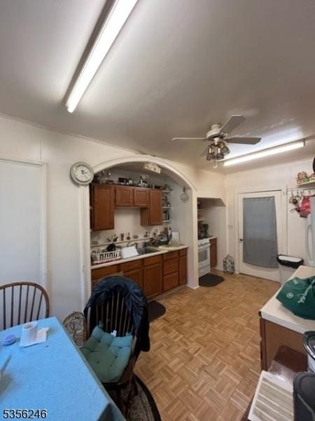 kitchen featuring brown cabinets, ceiling fan, light countertops, electric range, and arched walkways