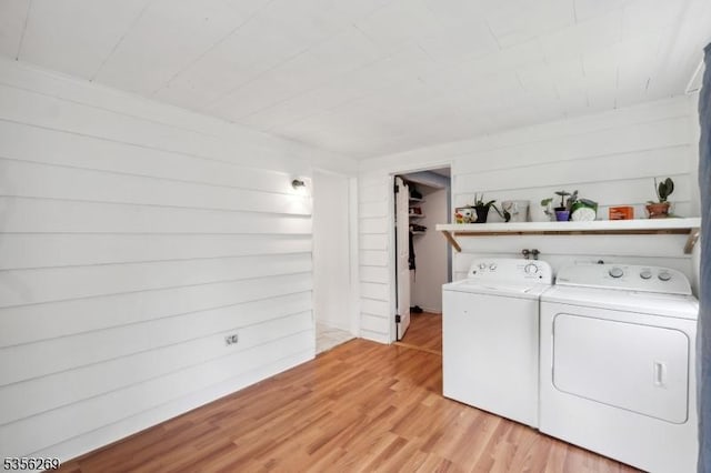 laundry room with separate washer and dryer, light wood-style flooring, and wood walls