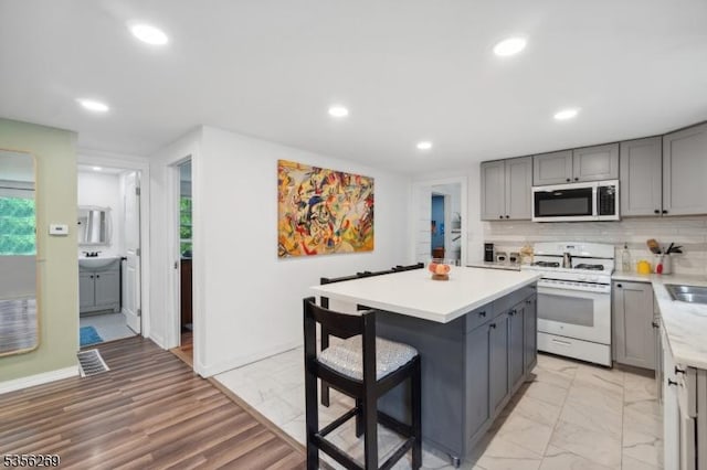 kitchen with white gas stove, stainless steel microwave, gray cabinetry, recessed lighting, and light countertops