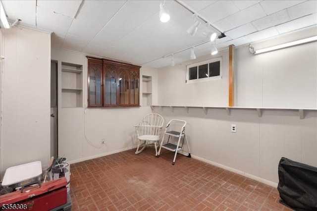 finished basement featuring brick patterned flooring, baseboards, and track lighting