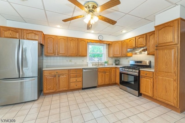 kitchen featuring stainless steel appliances, under cabinet range hood, a sink, light countertops, and brown cabinetry