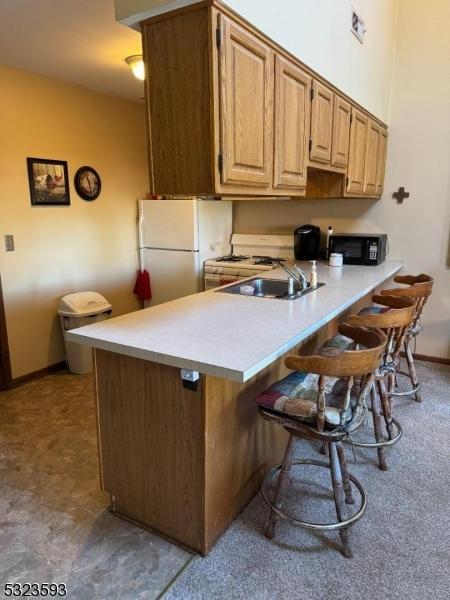 8 Le Touquet Unit 4, Vernon Twp, NJ 07462 - kitchen with freestanding refrigerator, a sink, black microwave, a breakfast bar, and light countertops