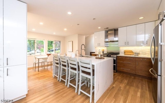 kitchen featuring wall chimney exhaust hood, stainless steel appliances, a sink, light wood finished floors, and recessed lighting