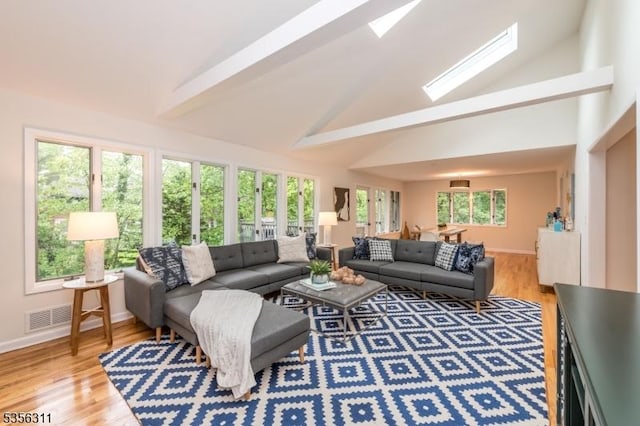 living area featuring high vaulted ceiling, baseboards, light wood finished floors, a skylight, and beamed ceiling