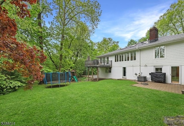 back of property featuring central AC, a playground, a trampoline, a lawn, and a chimney