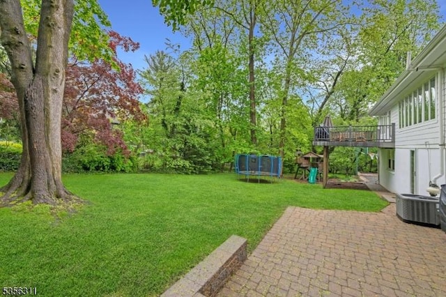 view of green lawn with a trampoline, a patio, cooling unit, a playground, and a wooden deck