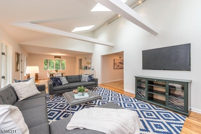 living area featuring a skylight, wood finished floors, rail lighting, vaulted ceiling, and baseboards